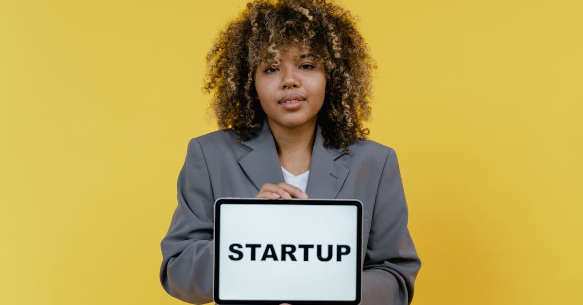 Portrait of a woman holding a tablet showing the word 'STARTUP' against a yellow background.