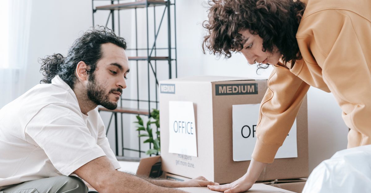 A couple packing and organizing office supplies into labeled boxes, preparing for relocation.